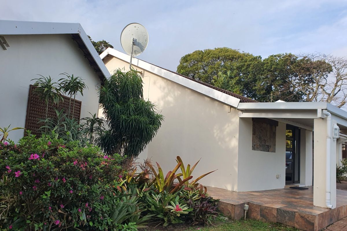A view of the rear exterior of the house featuring a tiled patio area, established garden landscaping, and exterior building fixtures.