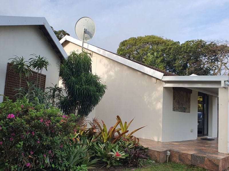 A view of the rear exterior of the house featuring a tiled patio area, established garden landscaping, and exterior building fixtures.