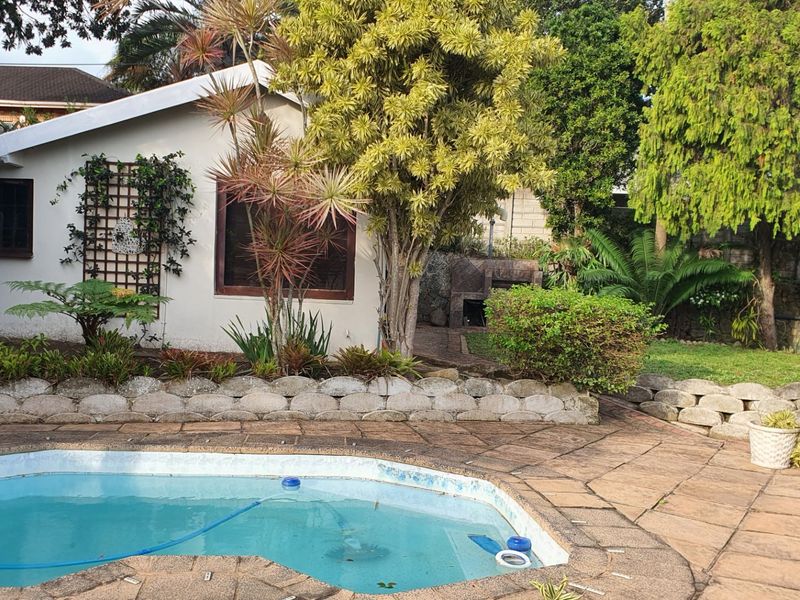 Outdoor pool area featuring stone paving, a built-in braai, and established garden landscaping, providing a functional space for outdoor entertainment.