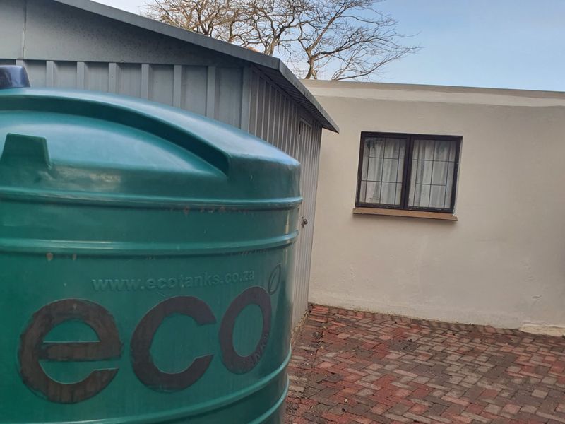 Rear exterior area featuring a large water storage tank, a metal storage shed, and brick paved ground surface.
