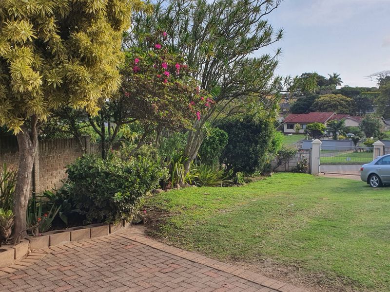 A well-maintained residential garden featuring brick paving, established trees, and a secure boundary wall with a metal gate.