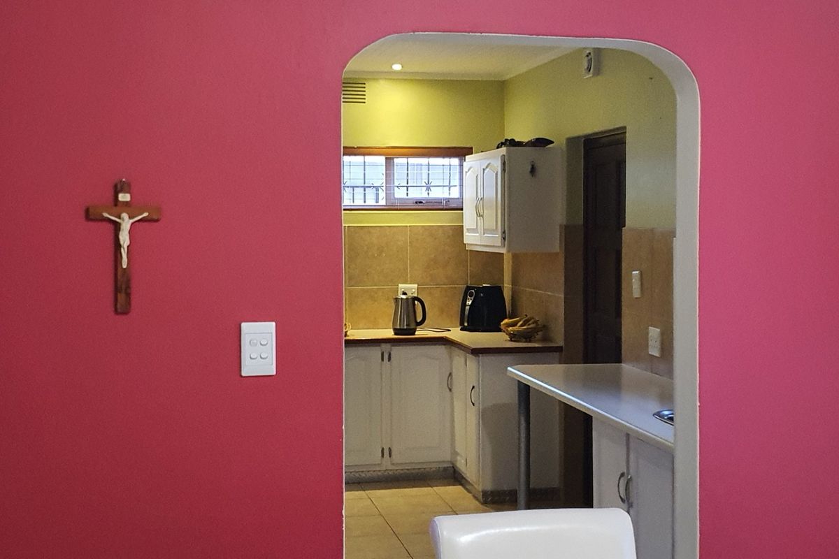 A view through an arched doorway into a functional kitchen featuring white cabinetry, tiled splashbacks, and laminate countertops.