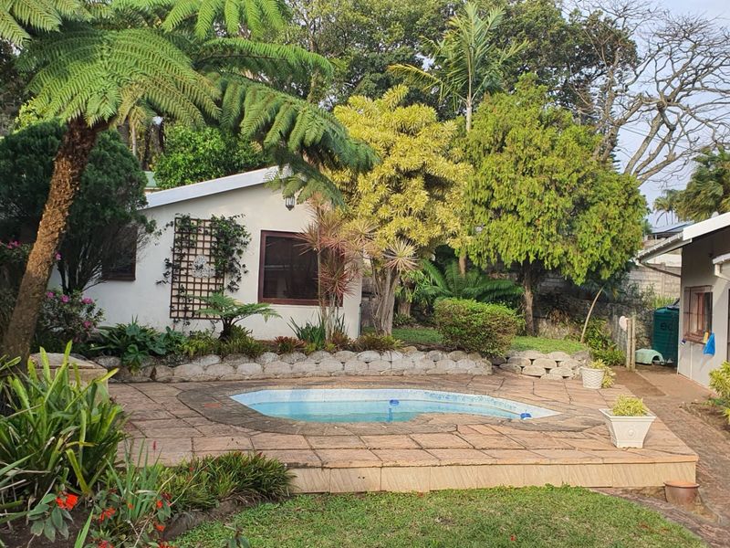 Outdoor pool area featuring a paved deck, established garden landscaping, and a retaining wall, providing a private space for relaxation.