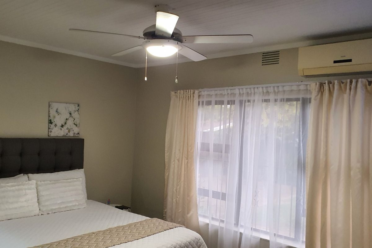 A bedroom featuring a ceiling fan and a wall-mounted split-system air conditioning unit.