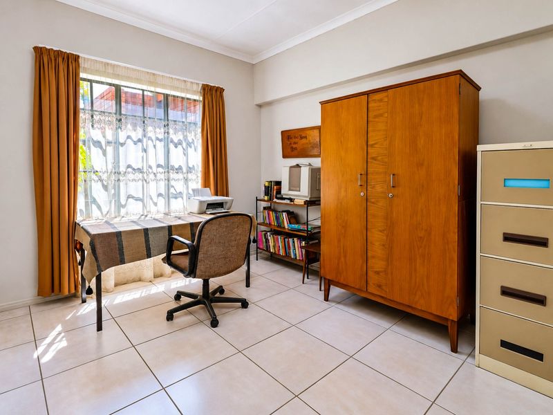 A functional home office space featuring neutral tiled flooring, a large window with security bars, and classic cove cornicing.