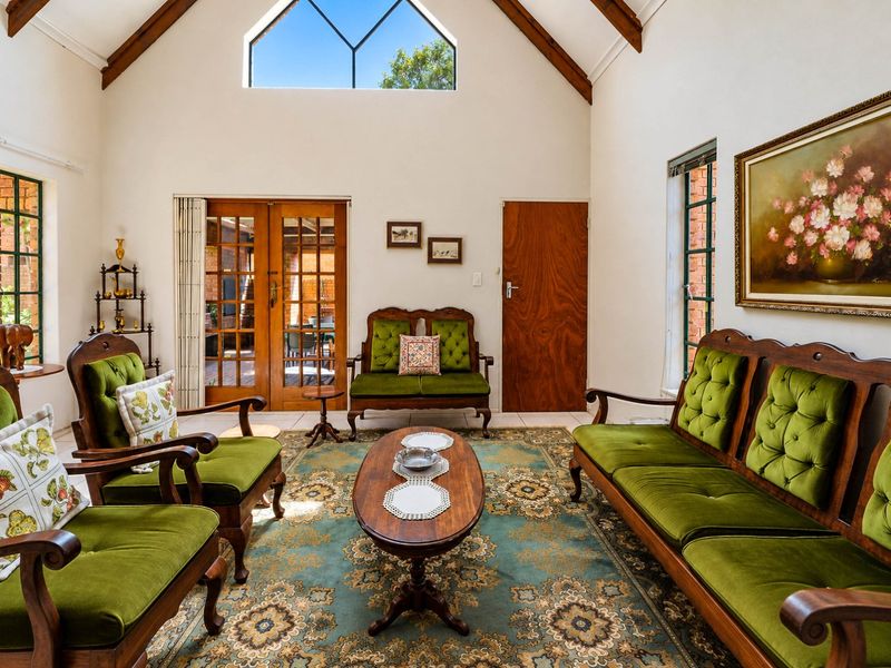 Spacious living room featuring a high vaulted ceiling with exposed timber beams, large feature window, and timber-framed glass doors leading to the patio.