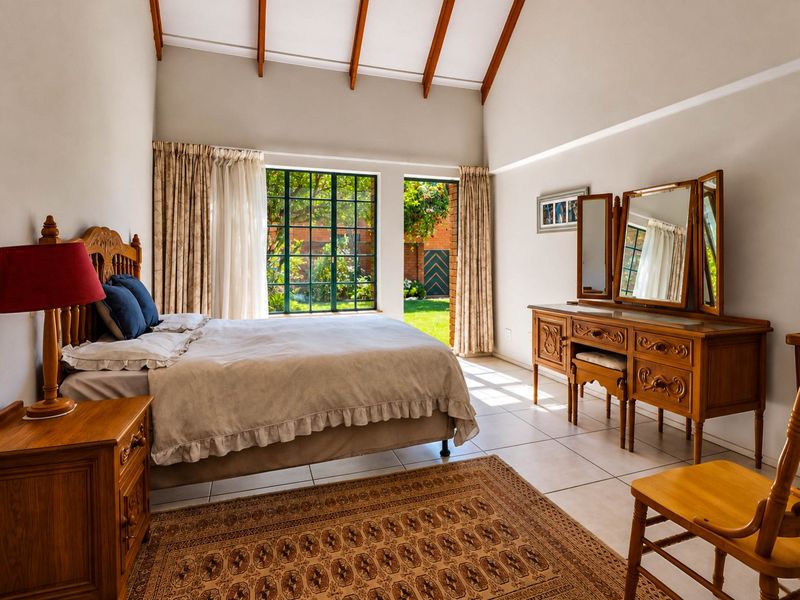 Spacious bedroom featuring high vaulted ceilings with exposed timber beams, tiled flooring, and direct access to a private garden through a glass door.