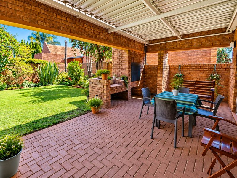 Covered outdoor patio featuring a built-in brick braai, brick paving, and direct access to a landscaped garden area.