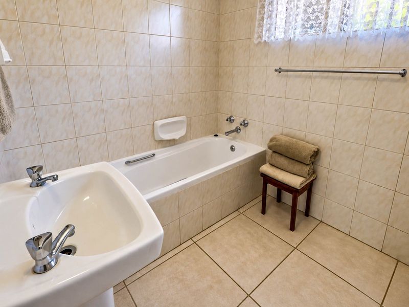 A functional bathroom featuring a bathtub, pedestal basin, and neutral floor-to-ceiling wall tiling, offering a clean and practical space.