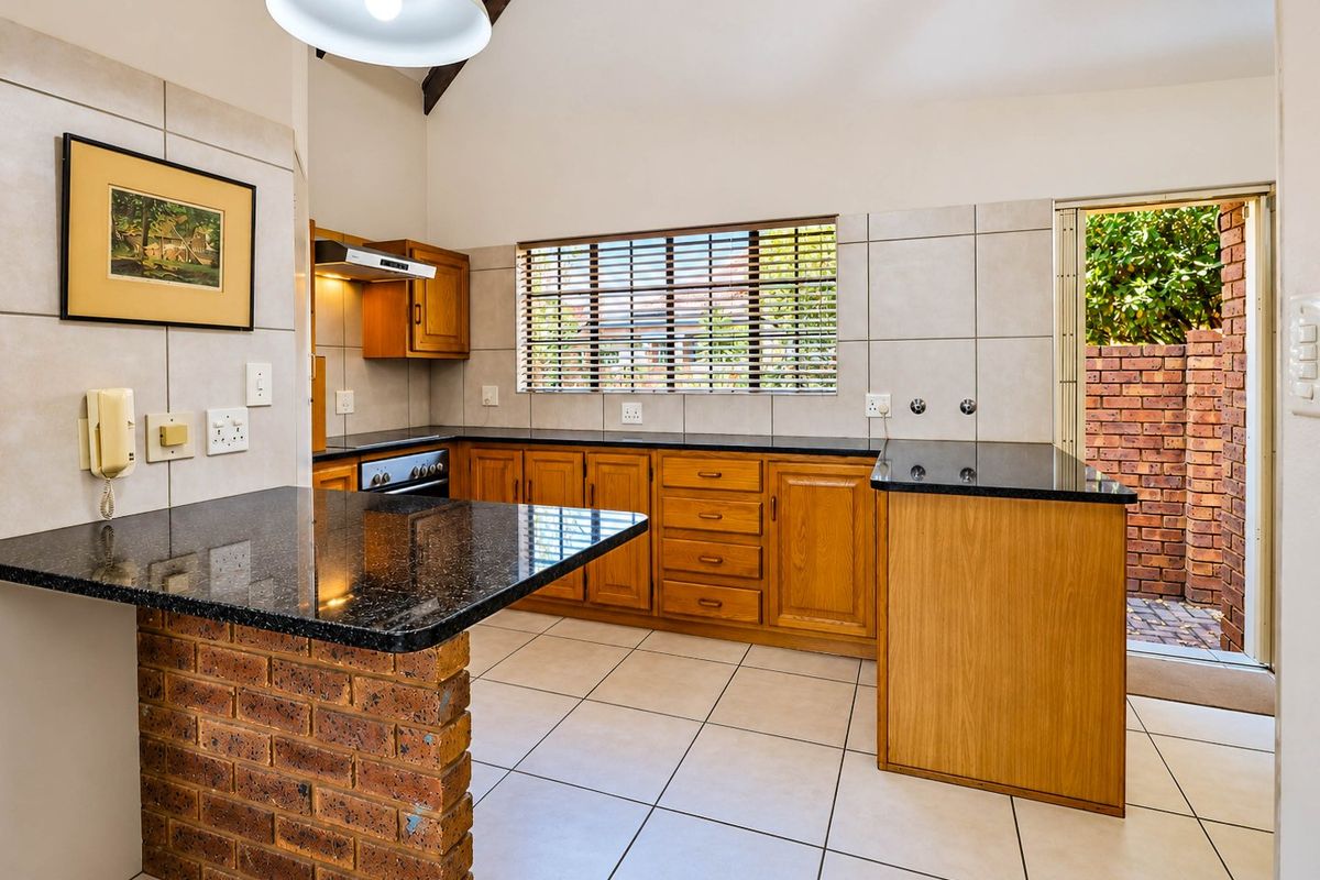 A functional kitchen featuring wooden cabinetry, granite countertops, a brick breakfast bar, and direct access to an outdoor area.