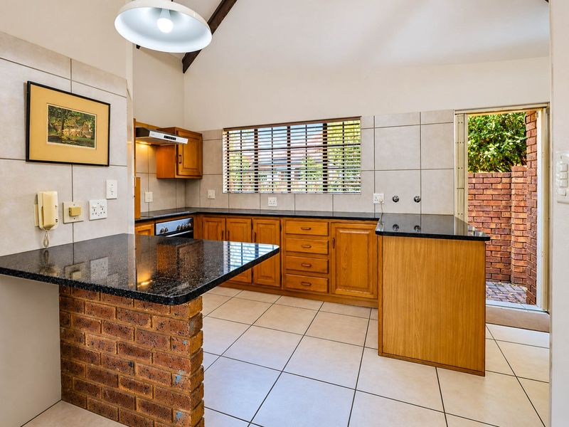 A functional kitchen featuring wooden cabinetry, granite countertops, a brick breakfast bar, and direct access to an outdoor area.