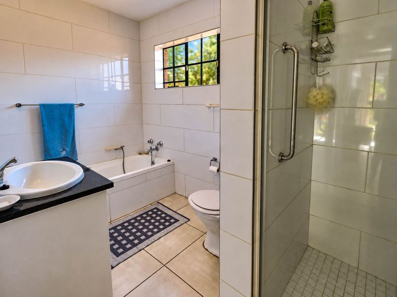 A functional bathroom featuring a built-in bathtub, separate shower enclosure, vanity basin, and toilet with neutral wall and floor tiling.