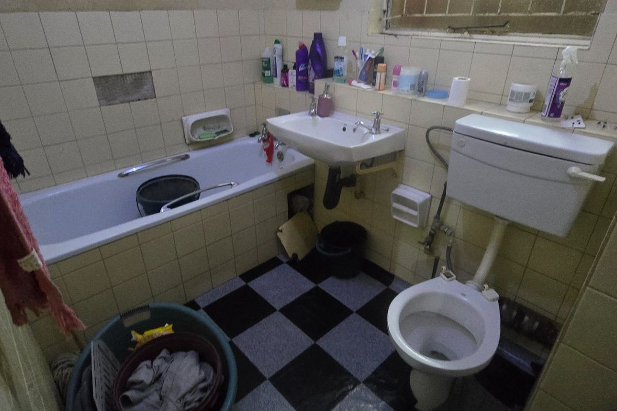 A dated bathroom featuring a bathtub, wall-mounted basin, and toilet with tiled finishes, requiring renovation and modernization of fixtures and surfaces.