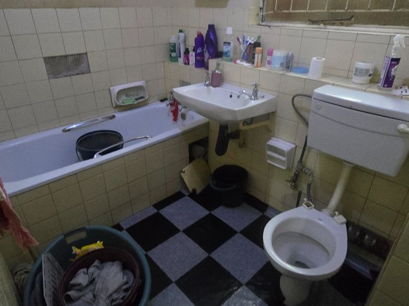 A dated bathroom featuring a bathtub, wall-mounted basin, and toilet with tiled finishes, requiring renovation and modernization of fixtures and surfaces.