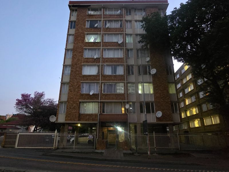 Exterior view of a multi-story brick apartment building featuring a gated entrance and security fencing at street level.