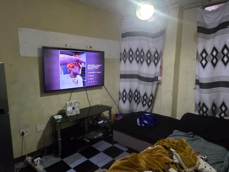 A small living area featuring wall-mounted television and tiled flooring, currently showing signs of wear and requiring cosmetic updates to improve the space.