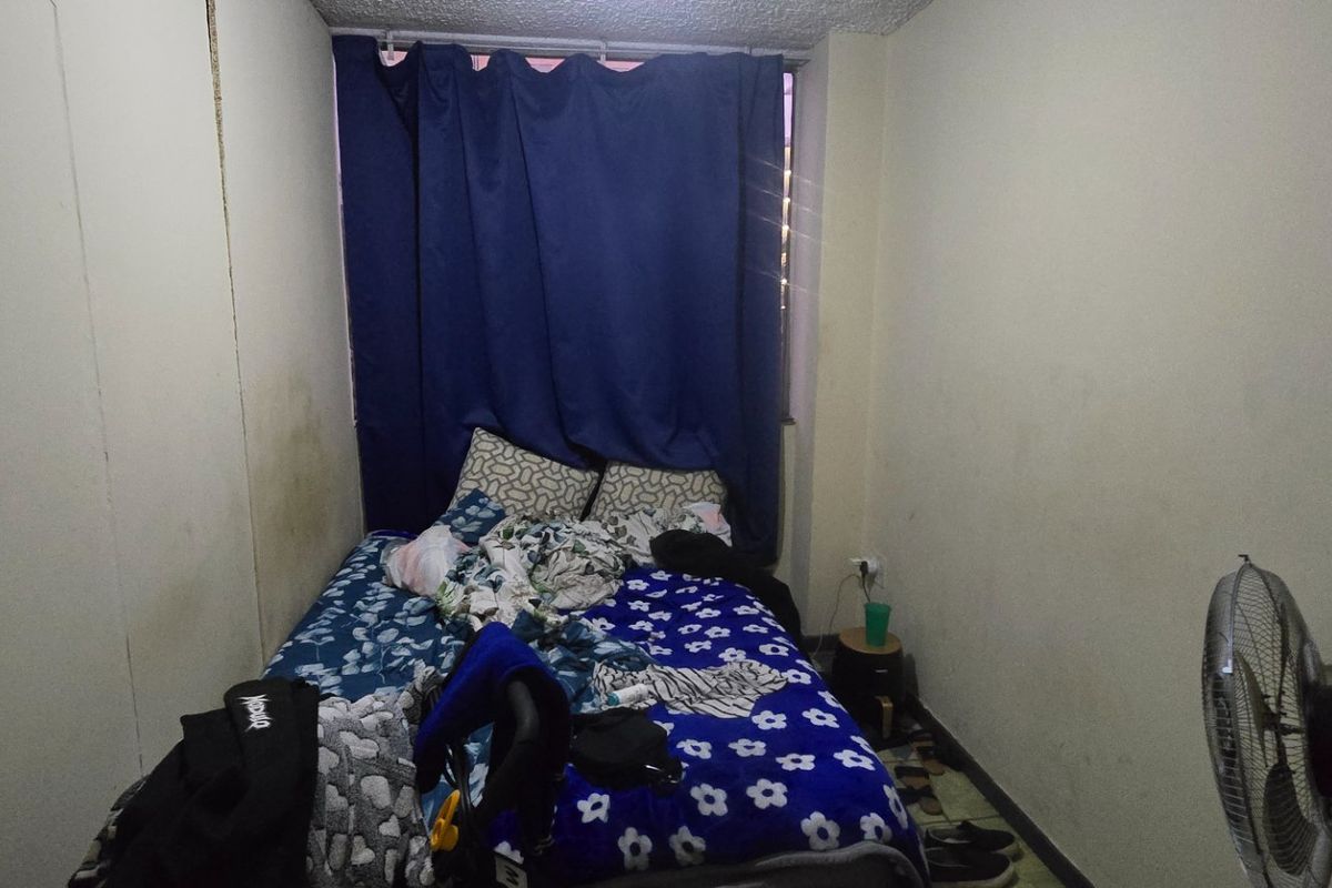 A compact bedroom featuring plain walls and a window covered by curtains, requiring cosmetic updates to improve the overall condition and appeal.