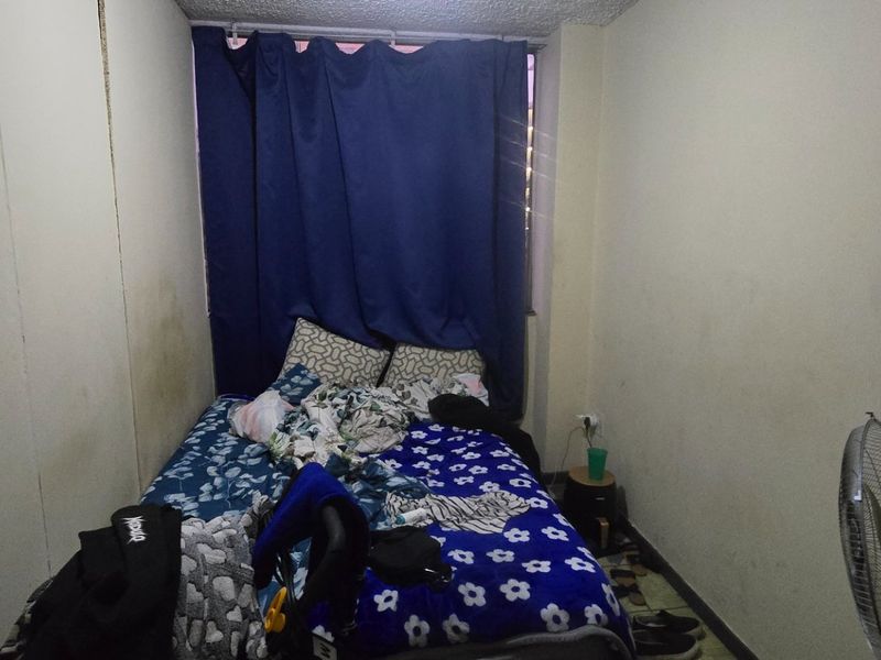A compact bedroom featuring plain walls and a window covered by curtains, requiring cosmetic updates to improve the overall condition and appeal.