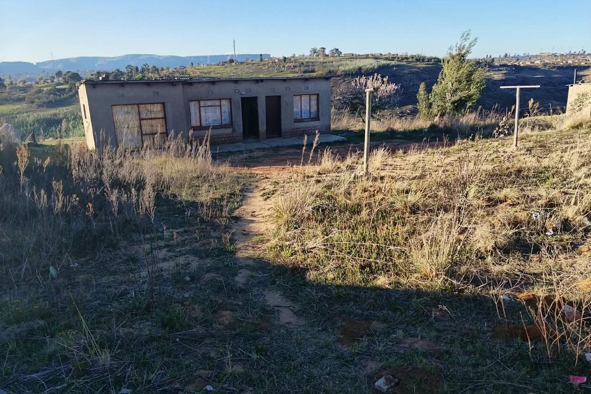 A single-story residential structure with a corrugated metal roof, situated on a rural plot with natural landscape and clear views of the surrounding terrain.