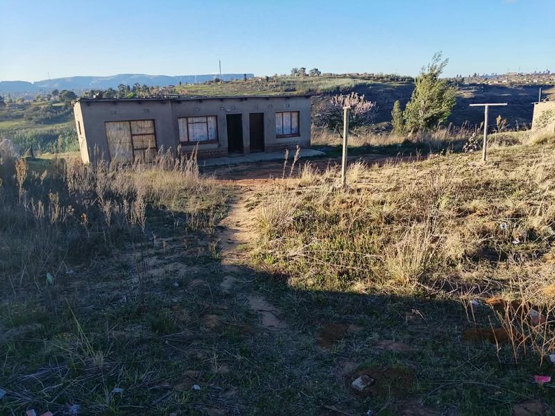 A single-story residential structure with a corrugated metal roof, situated on a rural plot with natural landscape and clear views of the surrounding terrain.