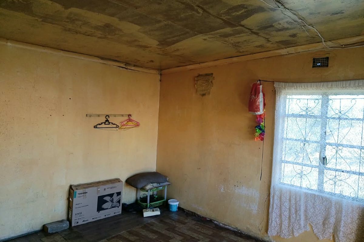 A vacant bedroom featuring a security gate on the window, showing significant signs of ceiling water damage and wall deterioration requiring renovation.