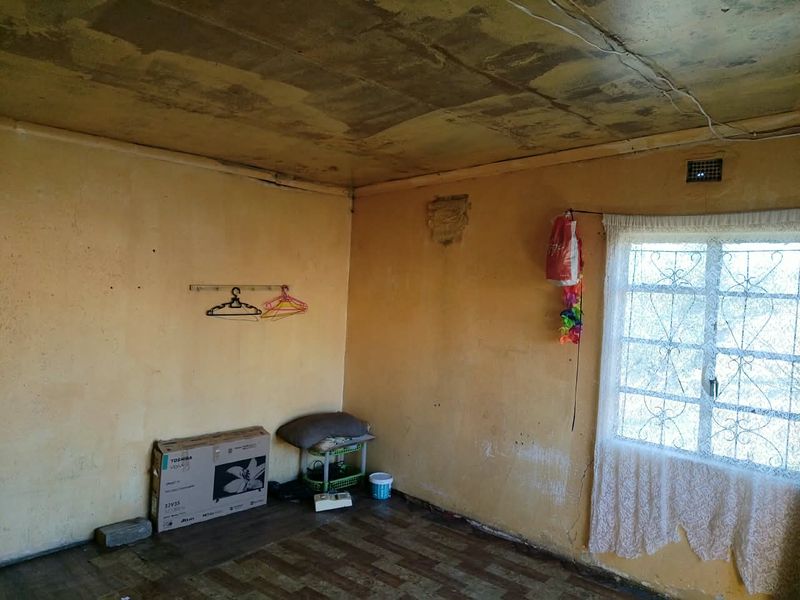 A vacant bedroom featuring a security gate on the window, showing significant signs of ceiling water damage and wall deterioration requiring renovation.