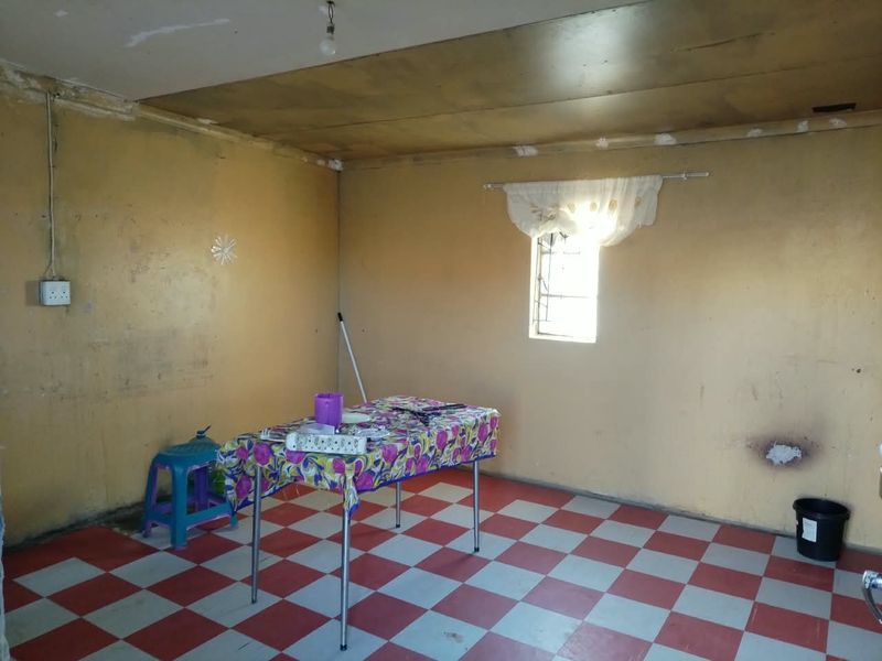 A vacant living area featuring checkered floor tiles, a window with security bars, and walls requiring cosmetic attention and refurbishment.