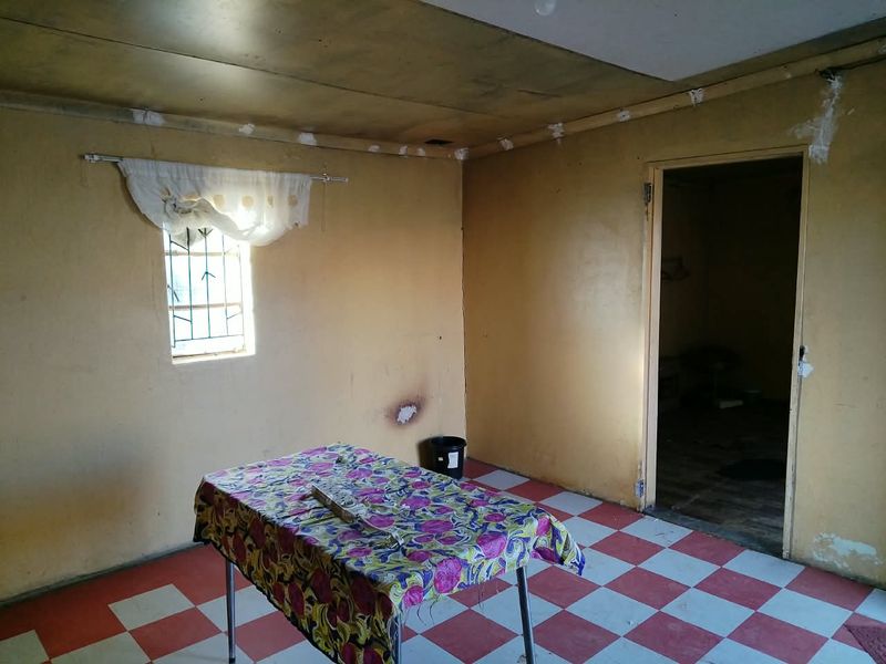A vacant living area featuring checkered floor tiles, security bars on the window, and walls requiring cosmetic attention and repainting.