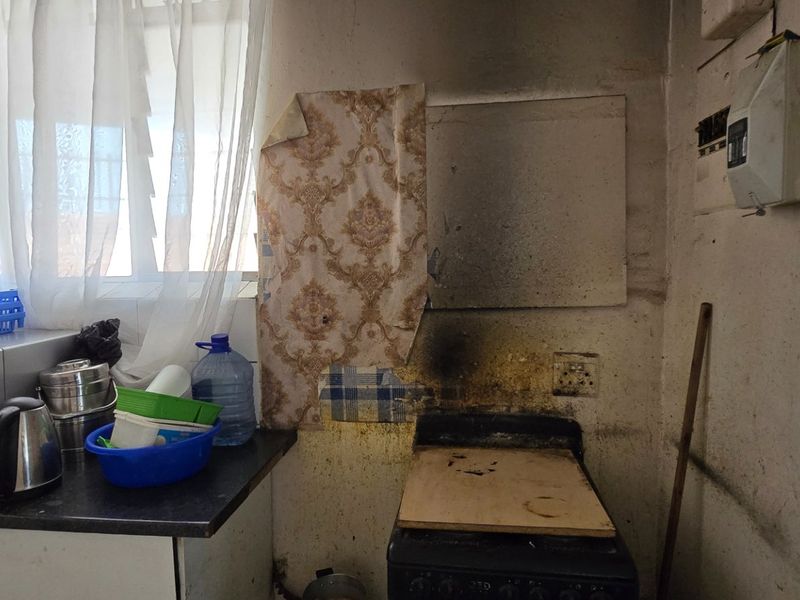 A kitchen area requiring significant renovation, featuring a freestanding stove, laminate countertop, and visible wall damage from heat or smoke exposure.