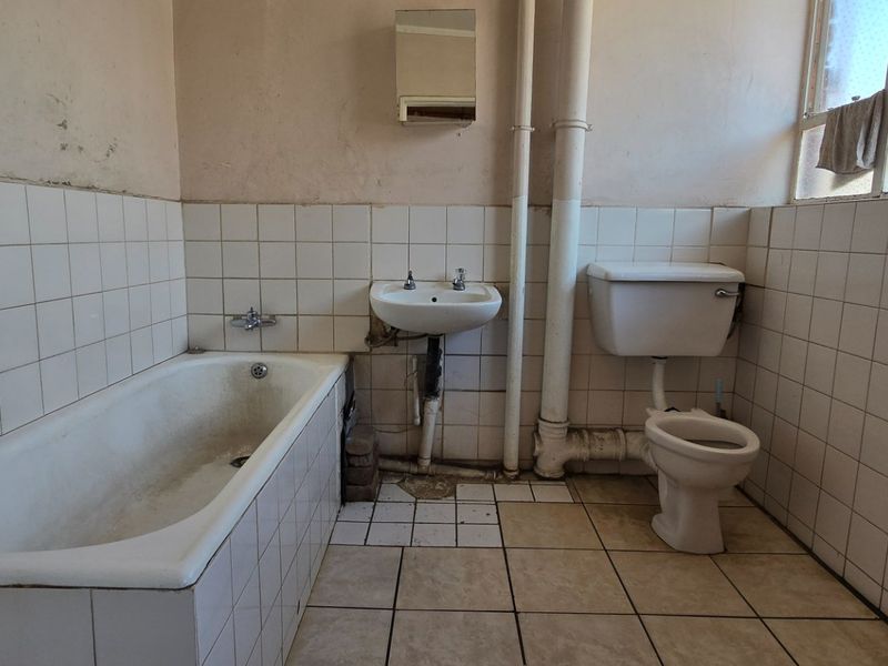 A dated bathroom featuring a bathtub, pedestal basin, and toilet with exposed plumbing, requiring renovation and modernization of finishes.