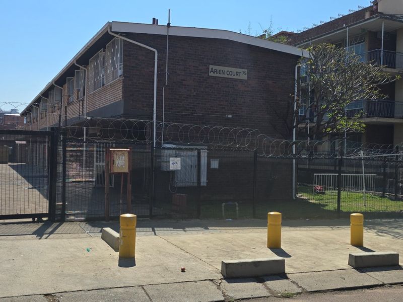 Exterior view of Arien Court apartment building featuring brick facade, secure gated entrance, and perimeter security fencing.