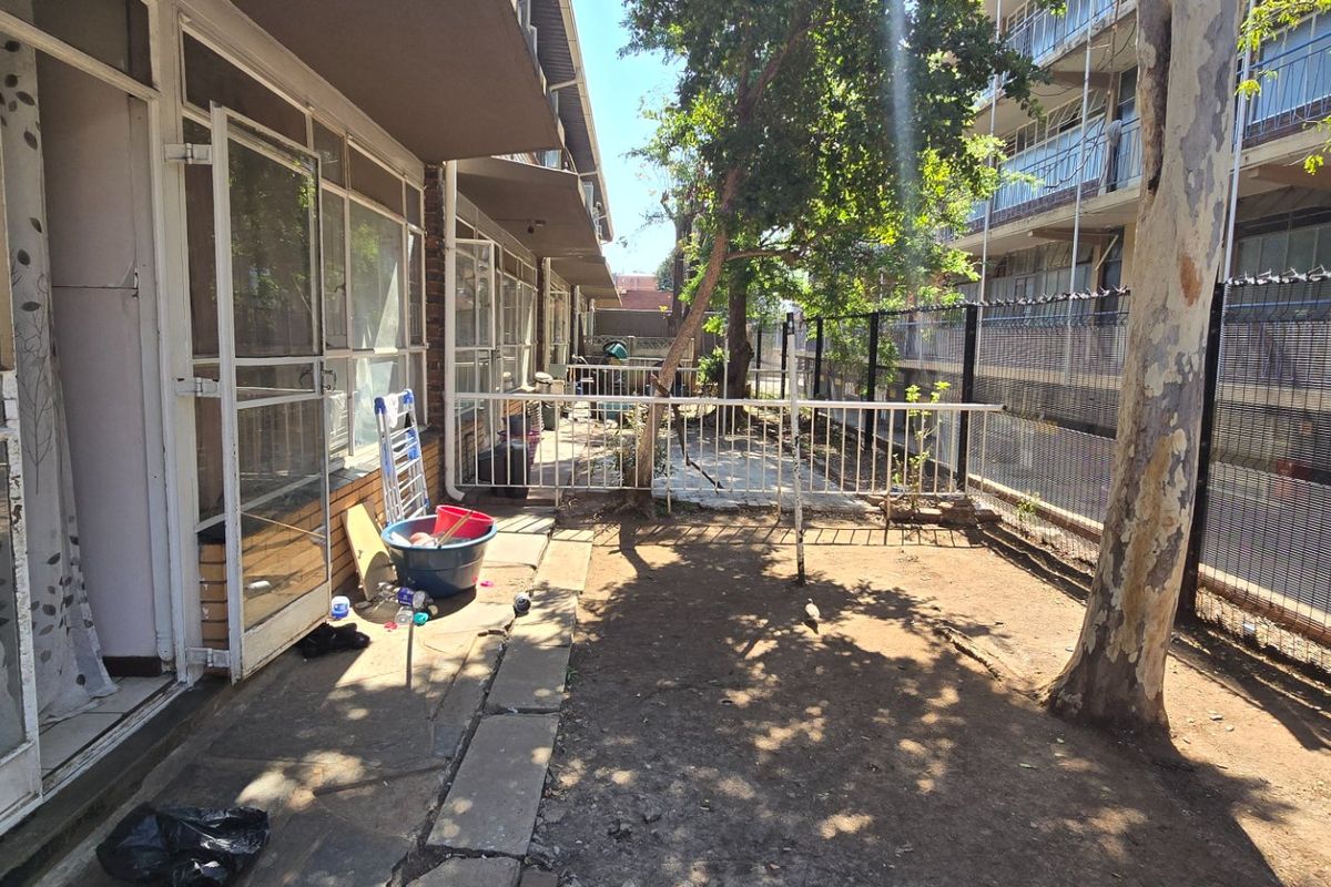 Rear exterior area of the apartment featuring a paved walkway, security gates, and a small garden space enclosed by metal fencing.