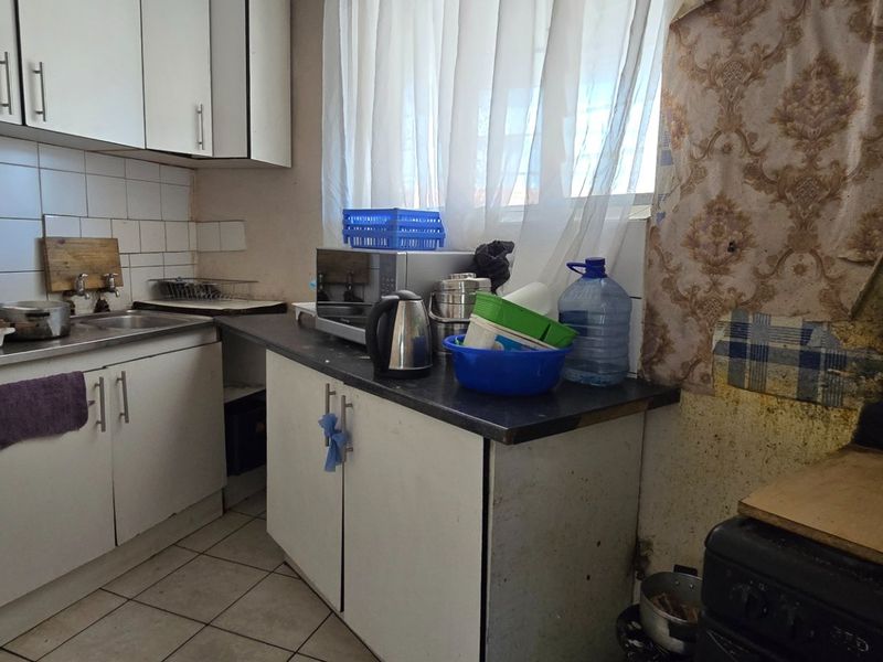 A compact kitchen featuring built-in cabinetry, tiled backsplash, and laminate countertops, currently requiring significant cosmetic updates and repairs to wall finishes.