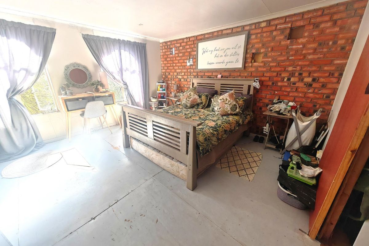 Spacious bedroom featuring an exposed brick feature wall, recessed lighting, and concrete flooring, offering a rustic aesthetic with potential for modern updates.