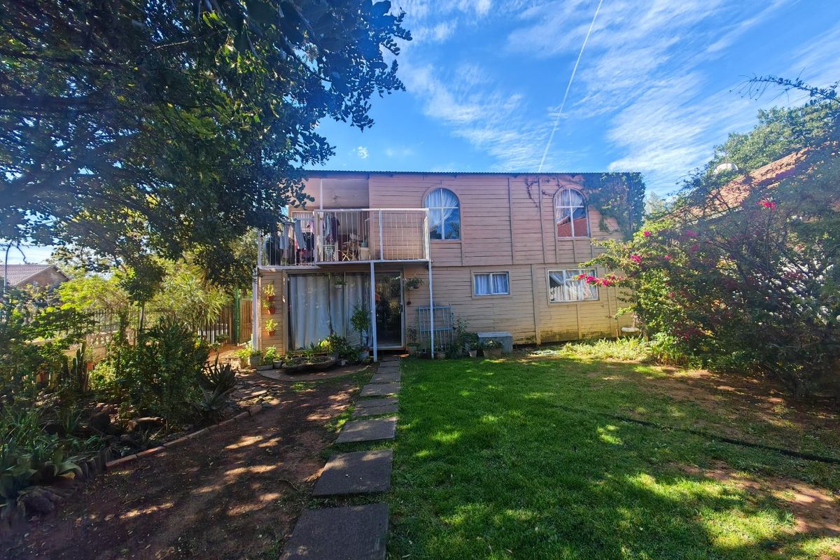 Rear view of a two-story timber-clad house featuring an upper-level balcony, arched windows, and a garden with a paved walkway.