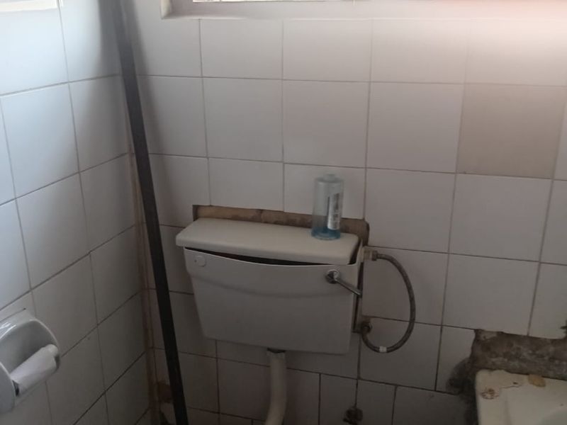 A bathroom featuring a toilet and tiled walls, currently showing significant signs of wear and missing tile sections requiring repair.