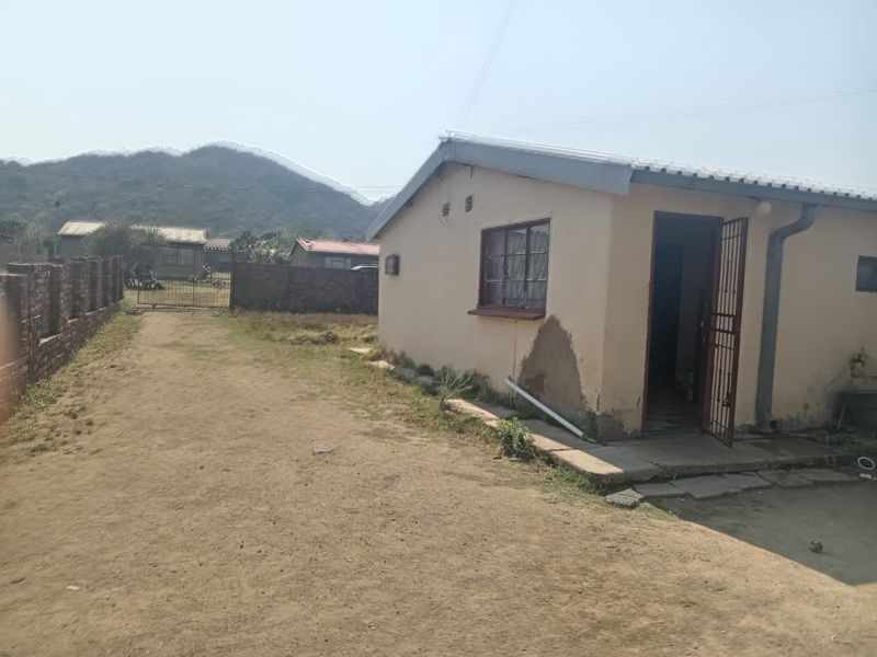 Rear view of a single-story house featuring a corrugated roof, security gate, and surrounding brick boundary wall with mountain views in the background.