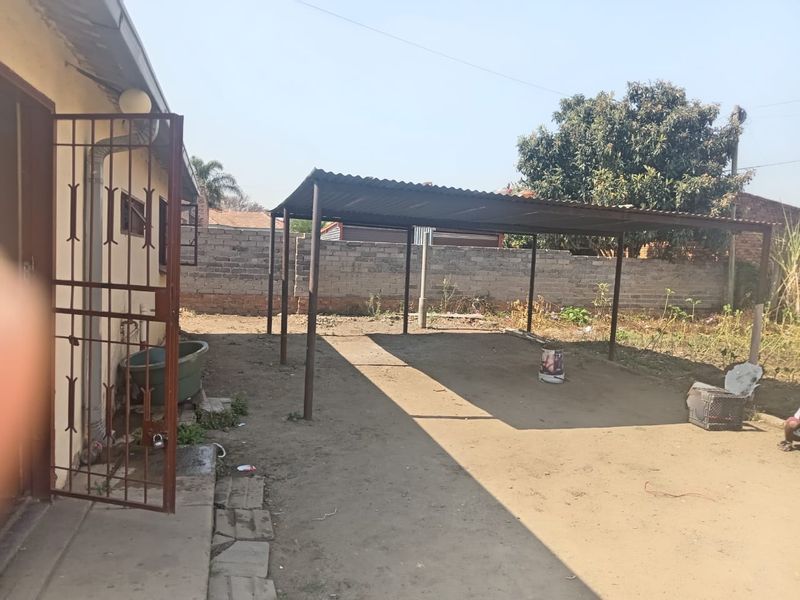 Rear exterior area featuring a metal carport structure, security gate, and brick boundary wall, offering potential for landscaping or outdoor improvement.