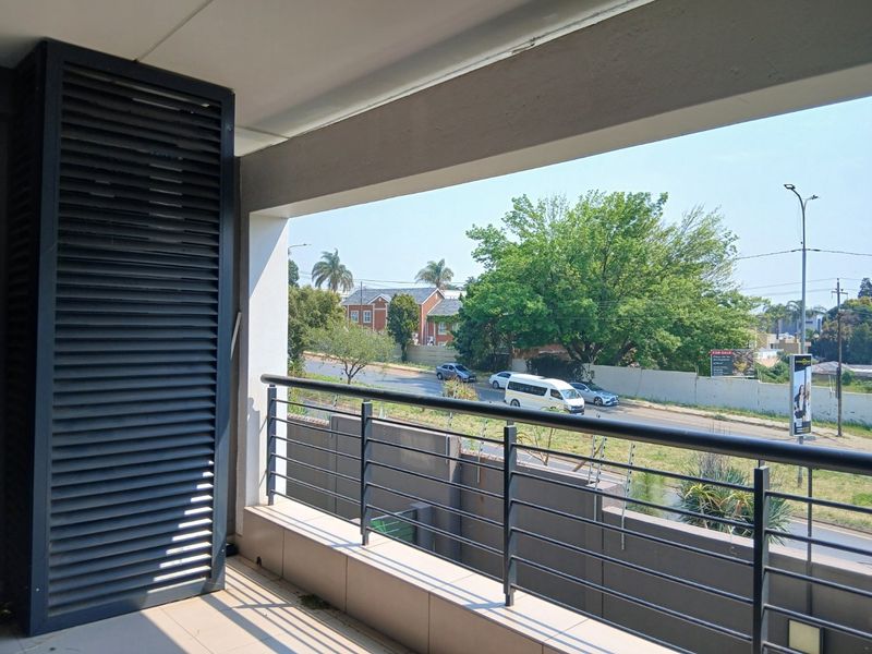 A covered balcony featuring tiled flooring, a metal balustrade, and a louvered privacy screen, offering an elevated view of the surrounding street and neighborhood.