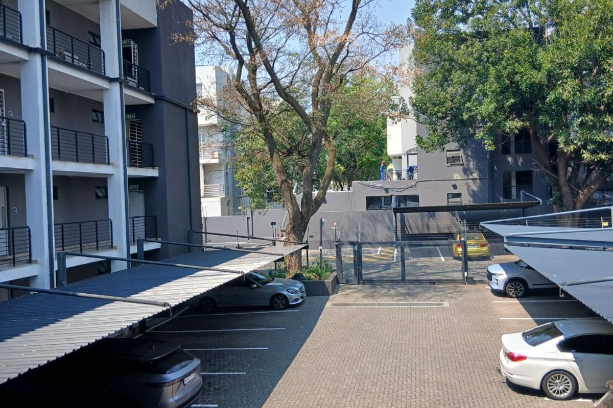 View of the apartment complex parking area featuring paved driveway, covered carports, and secure perimeter fencing.