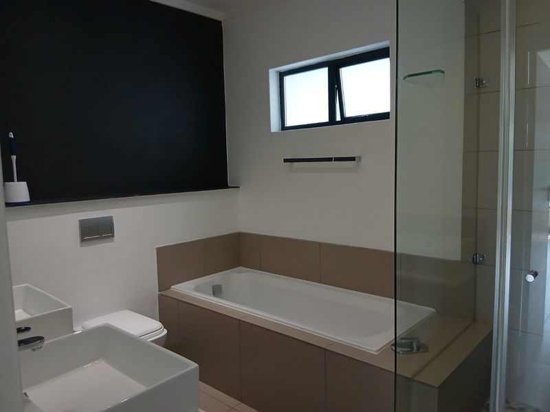 Modern bathroom featuring a built-in bathtub, glass shower enclosure, and dual vanity basins with contemporary fixtures and neutral tiling.