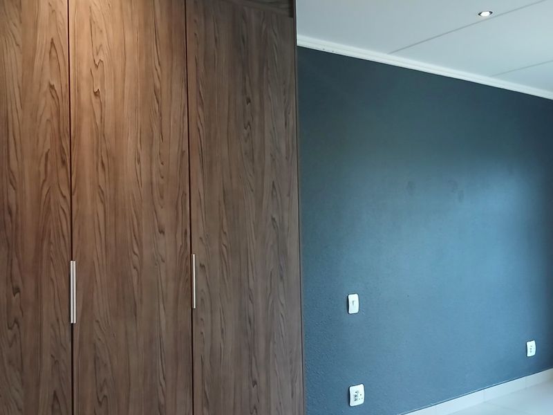 A clean, empty bedroom featuring modern dark wood built-in cupboards, tiled flooring, and recessed downlighting against a dark accent wall.