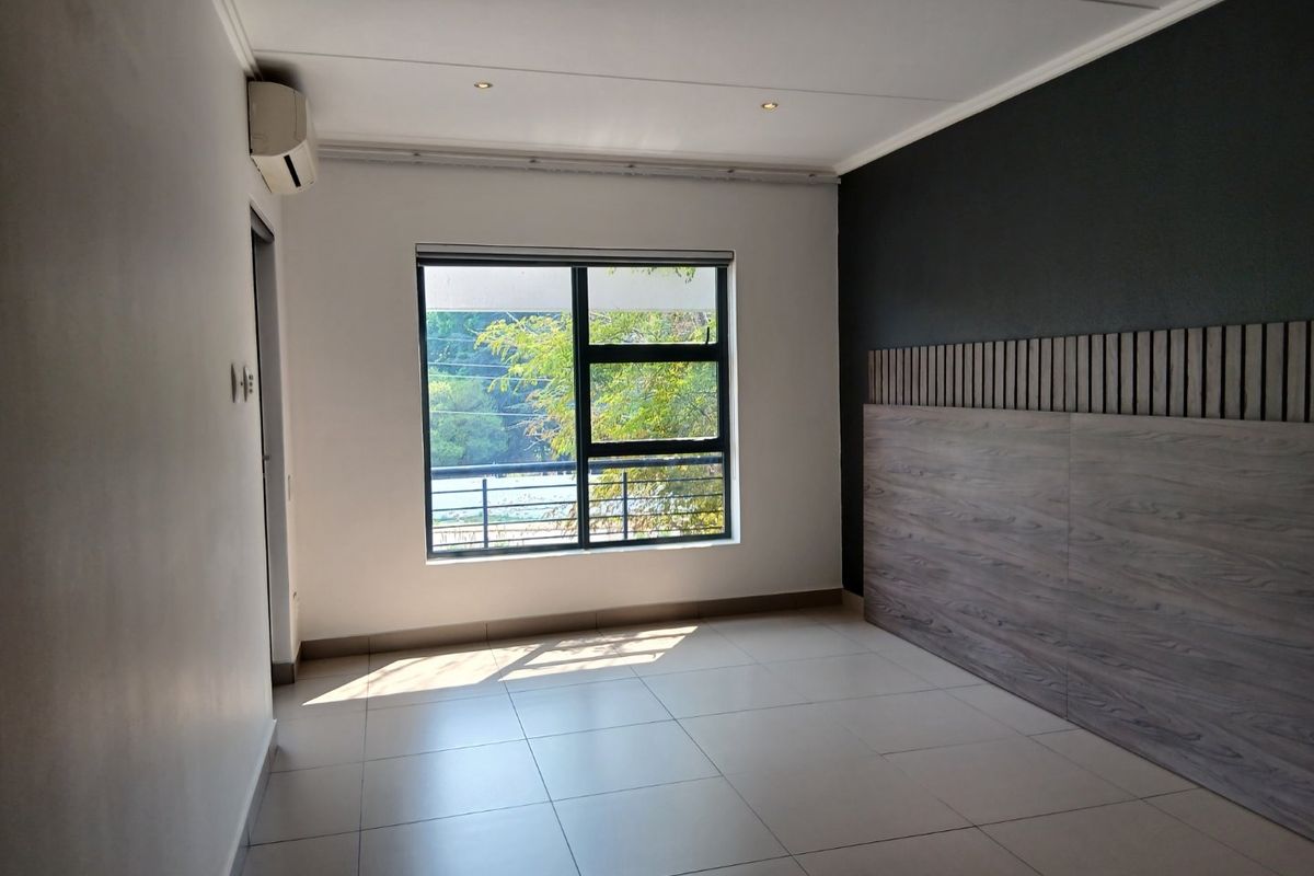 A bright, empty bedroom featuring tiled flooring, recessed lighting, an air conditioning unit, and a modern wood-look feature wall panel.