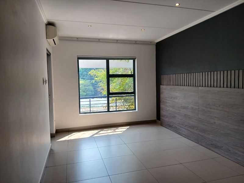 A bright, empty bedroom featuring tiled flooring, recessed lighting, an air conditioning unit, and a modern wood-look feature wall panel.