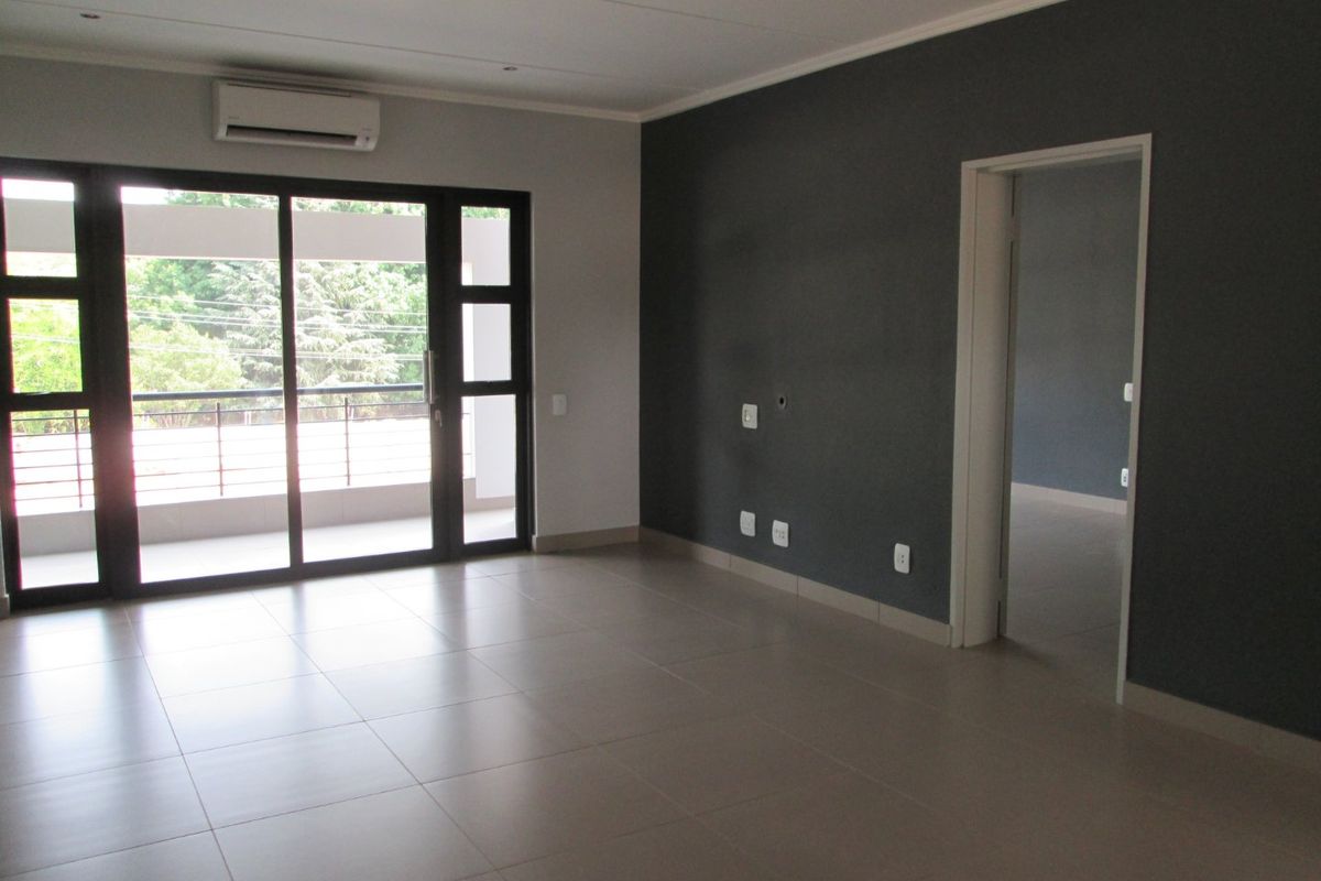 Spacious, empty living area featuring neutral tiled flooring, a dark accent wall, recessed lighting, and a sliding glass door leading to a balcony.