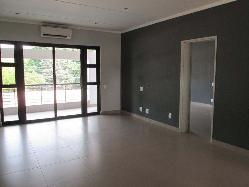 Spacious, empty living area featuring neutral tiled flooring, a dark accent wall, recessed lighting, and a sliding glass door leading to a balcony.