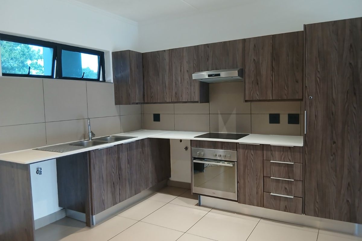 Modern kitchen featuring dark wood-grain cabinetry, integrated stainless steel appliances, sleek white countertops, and neutral tiled splashbacks in a clean, open layout.