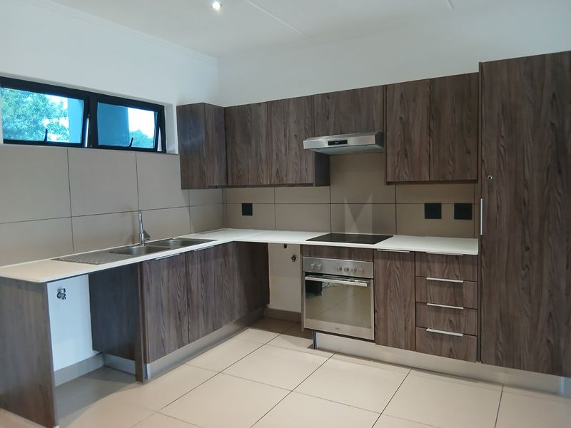 Modern kitchen featuring dark wood-grain cabinetry, integrated stainless steel appliances, sleek white countertops, and neutral tiled splashbacks in a clean, open layout.
