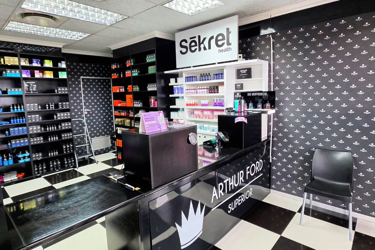 A commercial retail space featuring built-in shelving, a branded reception counter, checkered flooring, and a suspended ceiling with recessed lighting.