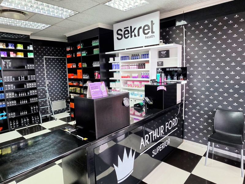 A commercial retail space featuring built-in shelving, a branded reception counter, checkered flooring, and a suspended ceiling with recessed lighting.